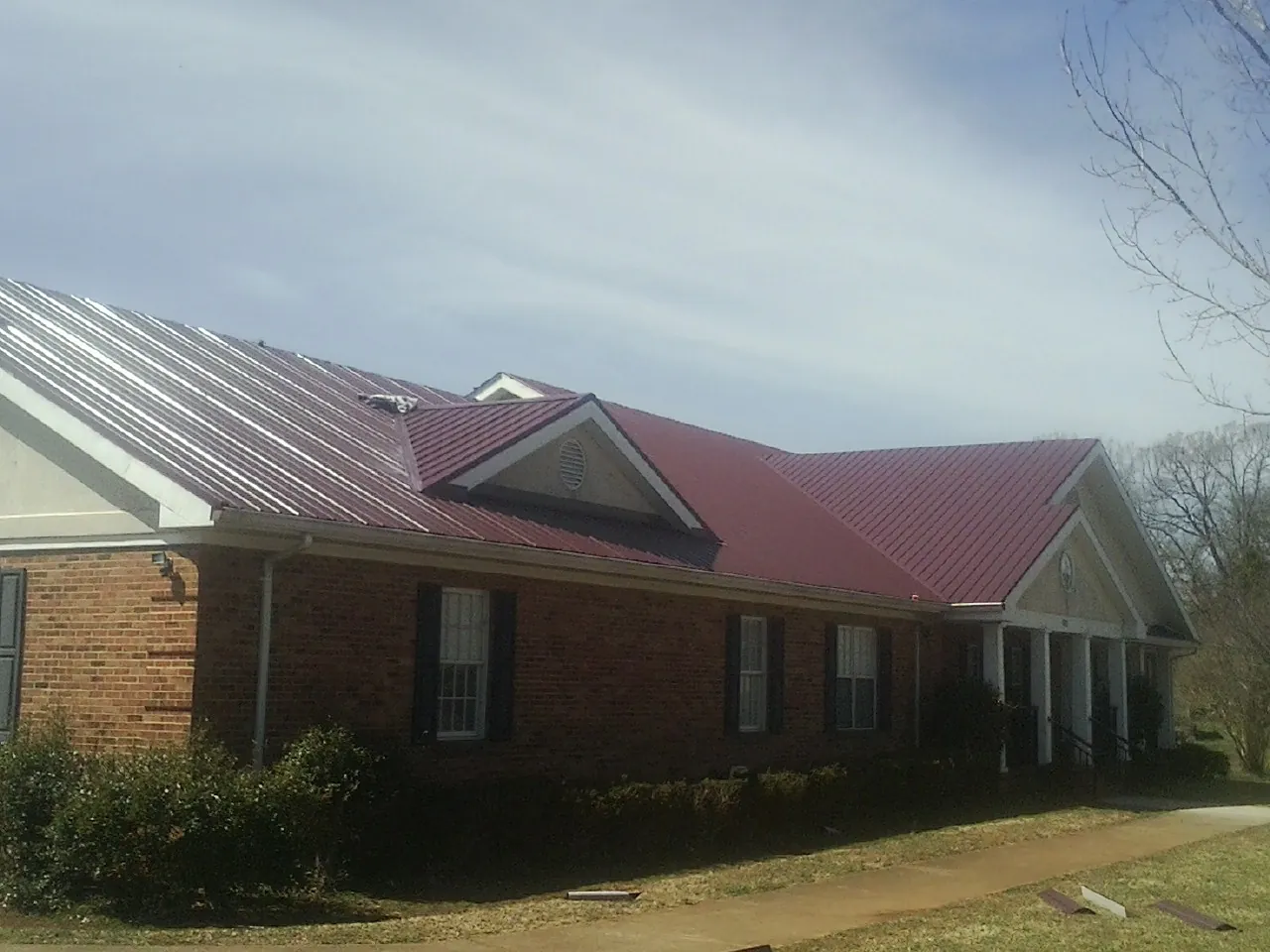 Red metal roof with gabled entries on a long brick building, from a Hail Damage Roof Repair job in Yorklyn