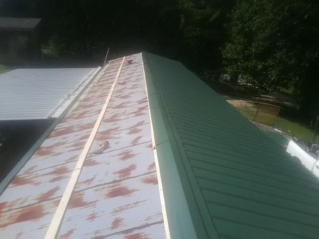 Old rusted panels beside newly installed green metal roofing — Wind Damage Roof Repair by Roofing Brothers in Yorklyn