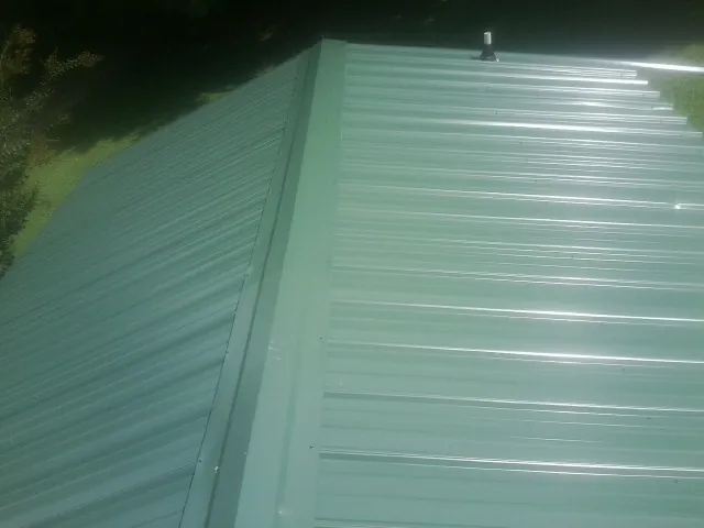 New green metal panels meeting at the ridge of a roof — Flat Roof Repair work by our crew in Yorklyn